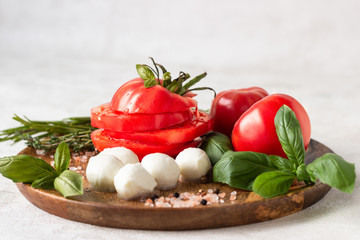 Mozzarella and tomato with basil leaves, rosemary and thyme on a wooden plate. Ingredients for Italian salad caprese.  Copy space