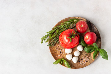 Mozzarella and tomato with basil leaves, rosemary and thyme on a wooden plate. Ingredients for Italian salad caprese.  Copy space