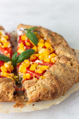 Homemade rustic open pie (galette) with tomato and sweet corn with fresh basil and greek yogurt on white background.