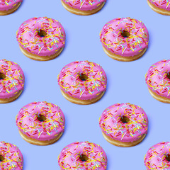 Fototapeta na wymiar Bright flat lay seamless pattern with donuts. Pink glazed donuts with colorful sugar sprinkles on violet blue background. Fashion minimalism style.