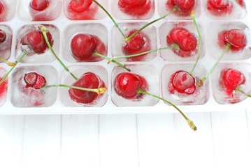 Naklejka na ściany i meble Closeup view of ice cubes tray with ripe wild cherries. Homemade frozen cherries.
