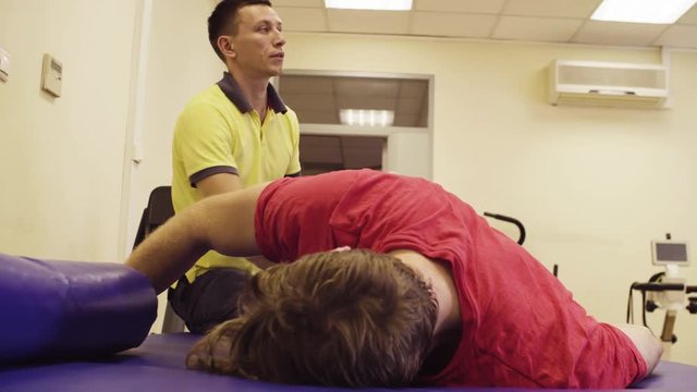 Portrait of a doctor physiotherapist doing stretching exercises for young disabled man at the rehabilitation center. The doctor's face is calm and focused