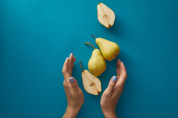 cropped image of woman holding hands near pears above blue surface