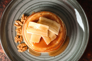 Tasty pancakes with walnuts and sliced banana on plate