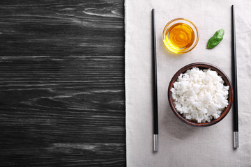 Bowls with boiled white rice, oil and chopsticks on wooden table