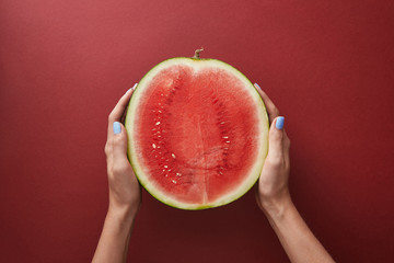 cropped image of woman holding half of watermelon above red surface