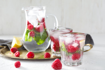 Glasses and jug of fresh raspberry mojito on white table