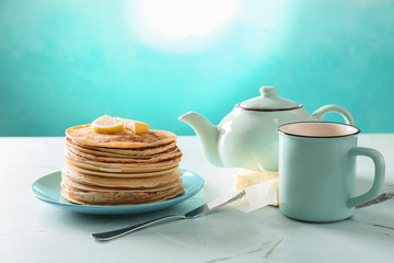 Plate with stack of delicious thin pancakes, butter and tea on light table