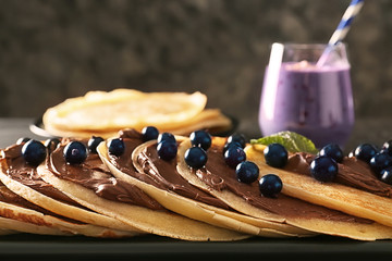 Delicious thin pancakes with berries and chocolate paste on plate, closeup