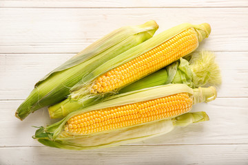 Fresh corn cobs on white wooden table