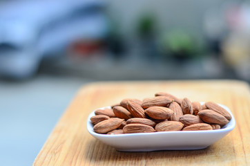 Salted roast organic almonds on a white plate on wood background