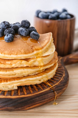 Board with tasty pancakes and blueberries on wooden table, closeup