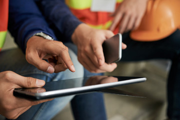 Crop hands of engineers pointing at tablet screen while browsing it during break