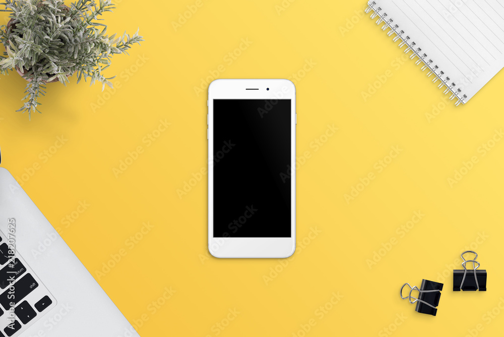 Aufkleber Simple, flat scene with white smart phone on yellow desk. Blank screen for app or responsive web site promotion. Laptop computer, plant, notepad and clips beside. Flat lay.