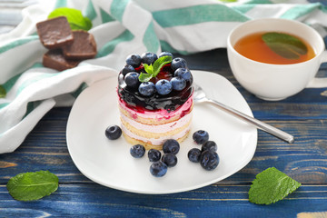Plate with delicious blueberry dessert and cup of tea on wooden table