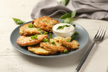 Plate with zucchini pancakes and sauce on wooden table