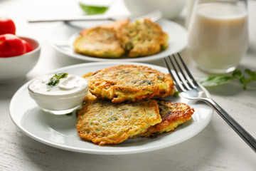Plate with zucchini pancakes and sauce on wooden table