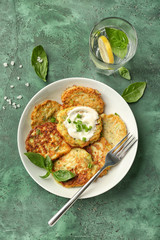 Plate with zucchini pancakes and glass of water on table