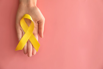 Woman holding yellow ribbon on color background. Cancer awareness concept