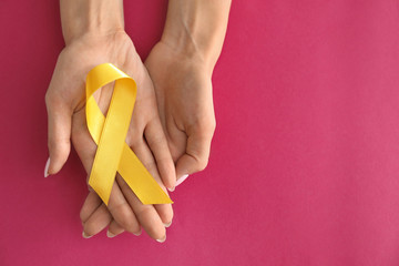 Woman holding yellow ribbon on color background. Cancer awareness concept