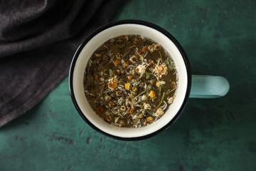 Cup of delicious camomile tea on green table, top view