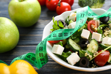 Plate with healthy fresh salad and measuring tape on wooden table. Diet concept