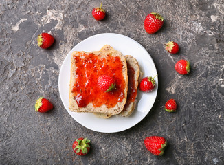 Plate with slices of bread and delicious strawberry jam on grunge table