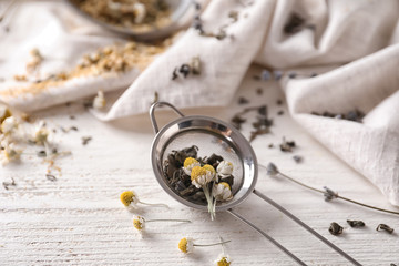 Obraz na płótnie Canvas Sieve with dried chamomile and tea leaves on white wooden table