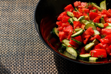 Salad of fresh tomatoes and cucumbers in a black plate on the table.