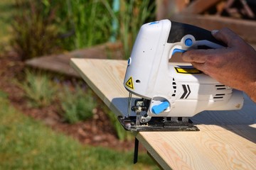 Cutting the boards with a jigsaw of a man's hand in the garden