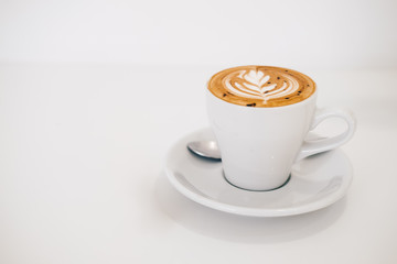 Close up white coffee cup with heart shape latte art foam on white wood table at cafe.