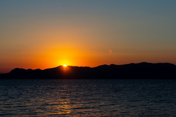 Sunset or sunrise over a mountain with an orange sky and water