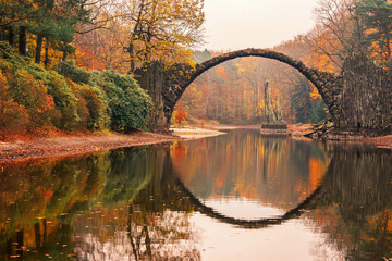 Rakotzbrücke (Rakotzbrucke, Teufelsbrücke) in Kromlau, Sachsen, Deutschland. Farbenfroher Herbst, Spiegelung der Brücke im Wasser bilden einen Kreis. Ungewöhnliche und interessante Orte in Deutschland.