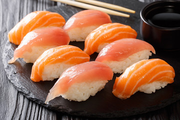 Freshly cooked sushi with salmon and tuna, soy sauce, chopsticks close-up on a black slate. horizontal