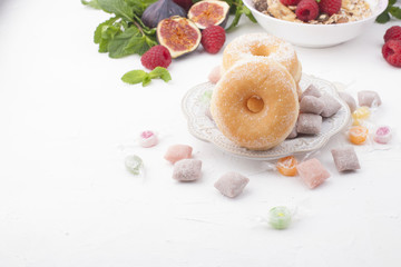 Delicious and healthy breakfast on a white background. Fruits, apples, raspberries, figs, fresh mint and donuts with sugar for a good morning. Free space for text, top view