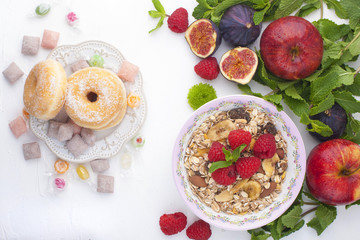 Delicious and healthy breakfast on a white background. Porridge of oatmeal, raspberry, honey, bananas, figs, mint fresh for a good morning. Free space for text, top view