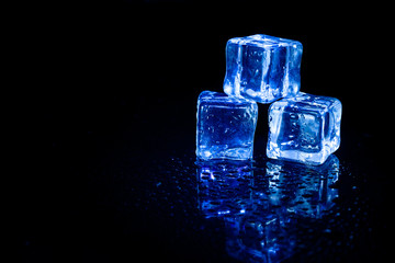 Blue ice cubes reflection on black table background.