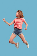 Fototapeta na wymiar Freedom in moving. Mid-air shot of pretty happy young woman jumping and gesturing against blue studio background. Runnin girl in motion or movement. Human emotions and facial expressions concept