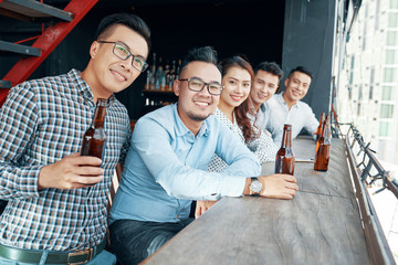 Perspective view of cheerful Asian men and woman sitting at counter near window with beer bottles...