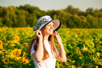 Summer portrait of happy young woman in hat with long hair in sunflower field enjoying nature