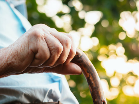 wrinkled old man' hands crossed on the stick. Close-up of a pensive grandfather sitting alone outdoors and rests on a cane.