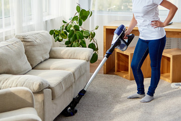 Young woman in white shirt and jeans cleaning carpet with vacuum cleaner in living room, copy space. Housework, cleanig and chores concept