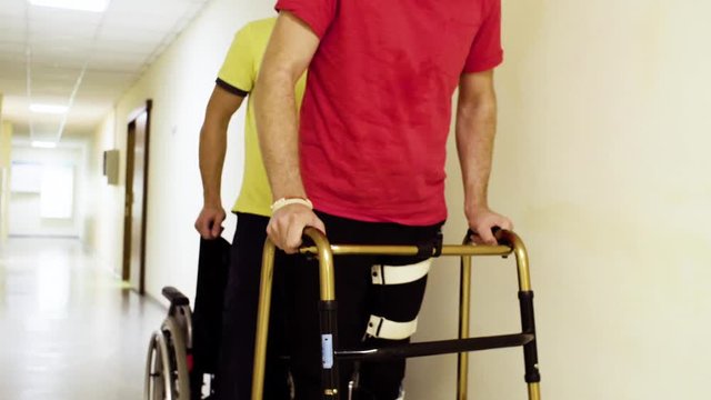 Legs of young disabled man in orthosis walking holding a walking frame through the corridor of the rehabilitation clinic.