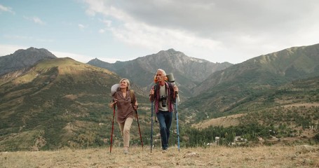 Active senior caucasian couple hiking in mountains with backpacks, enjoying their adventure 4k - Powered by Adobe