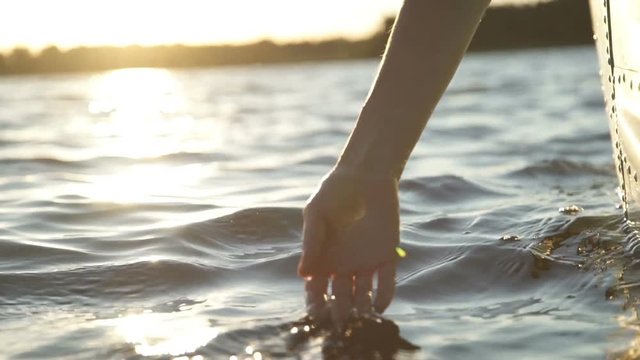 At sunset, close-up the hand of a girl moving through the water