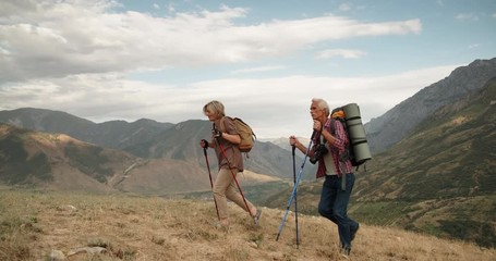 Active senior caucasian couple hiking in mountains with backpacks, enjoying their adventure 4k - Powered by Adobe