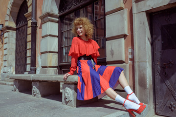Fototapeta na wymiar Young woman with curly hair in red retro dress. Walk around the city