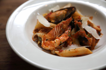 Penne pasta tomato sauce arabiata with seafood on wood background vintage style