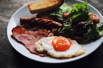 English breakfast  fried egg, ham,sausage, bacon,salad and toast on wood background in mystic light