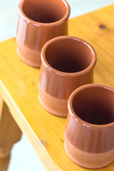 Set of traditional spanish red clay glazed earthenware cups on wooden table. Mediterranean kitchen interior decoration style local artisanal craftsmanship natural materials. Lifestyle image